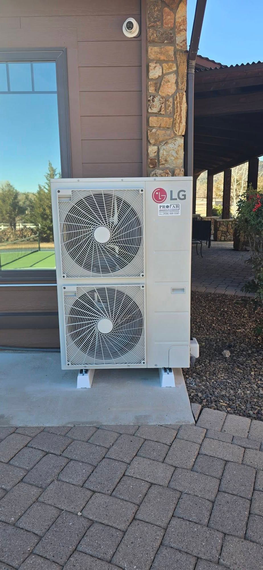 Outdoor LG air conditioning unit beside a building on a paved patio in sunlight