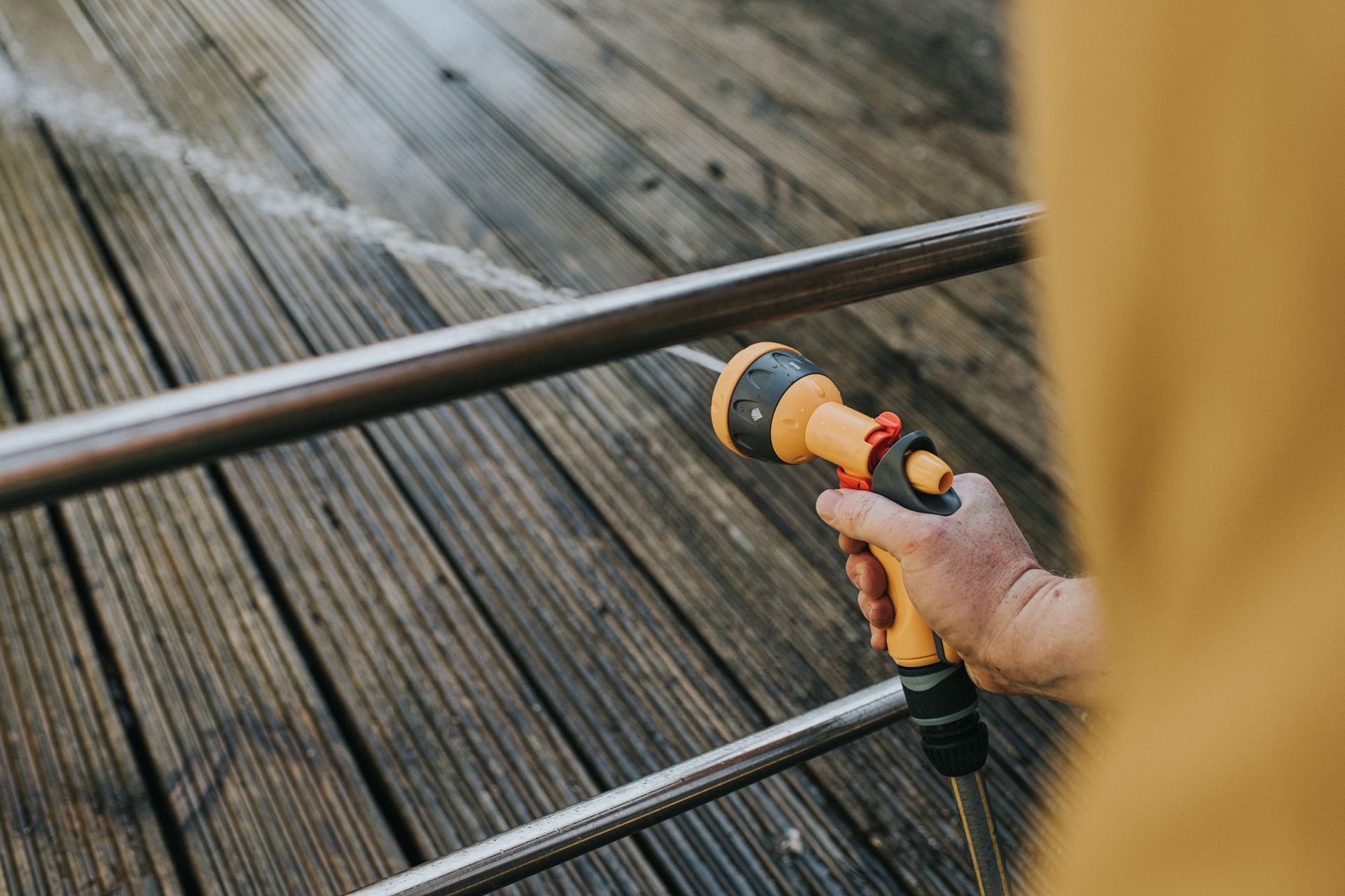 A person is using a hose to spray water on a wooden deck. A person is using a hose to spray water on a wooden deck.