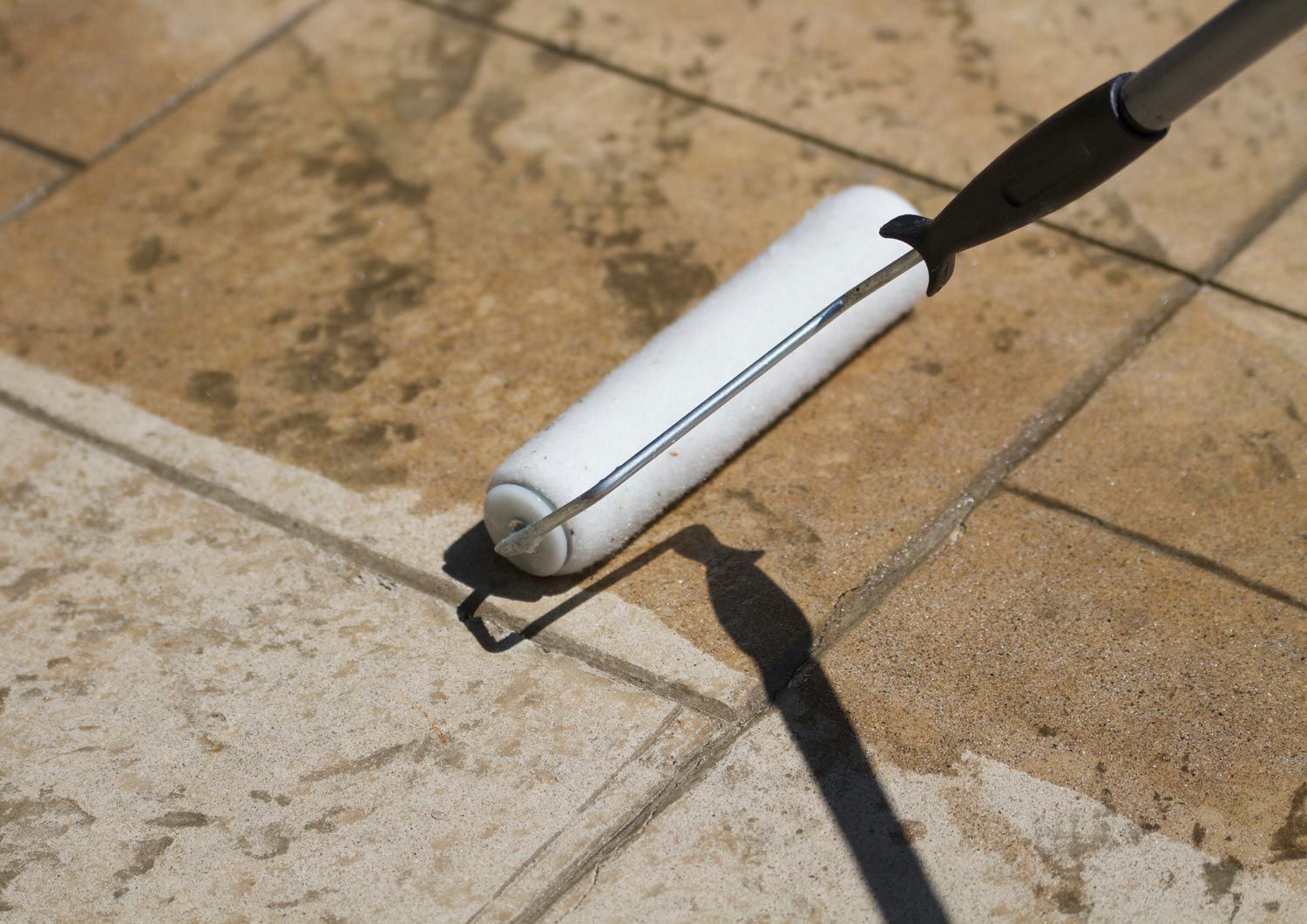 A white roller is being used to paint a tile floor