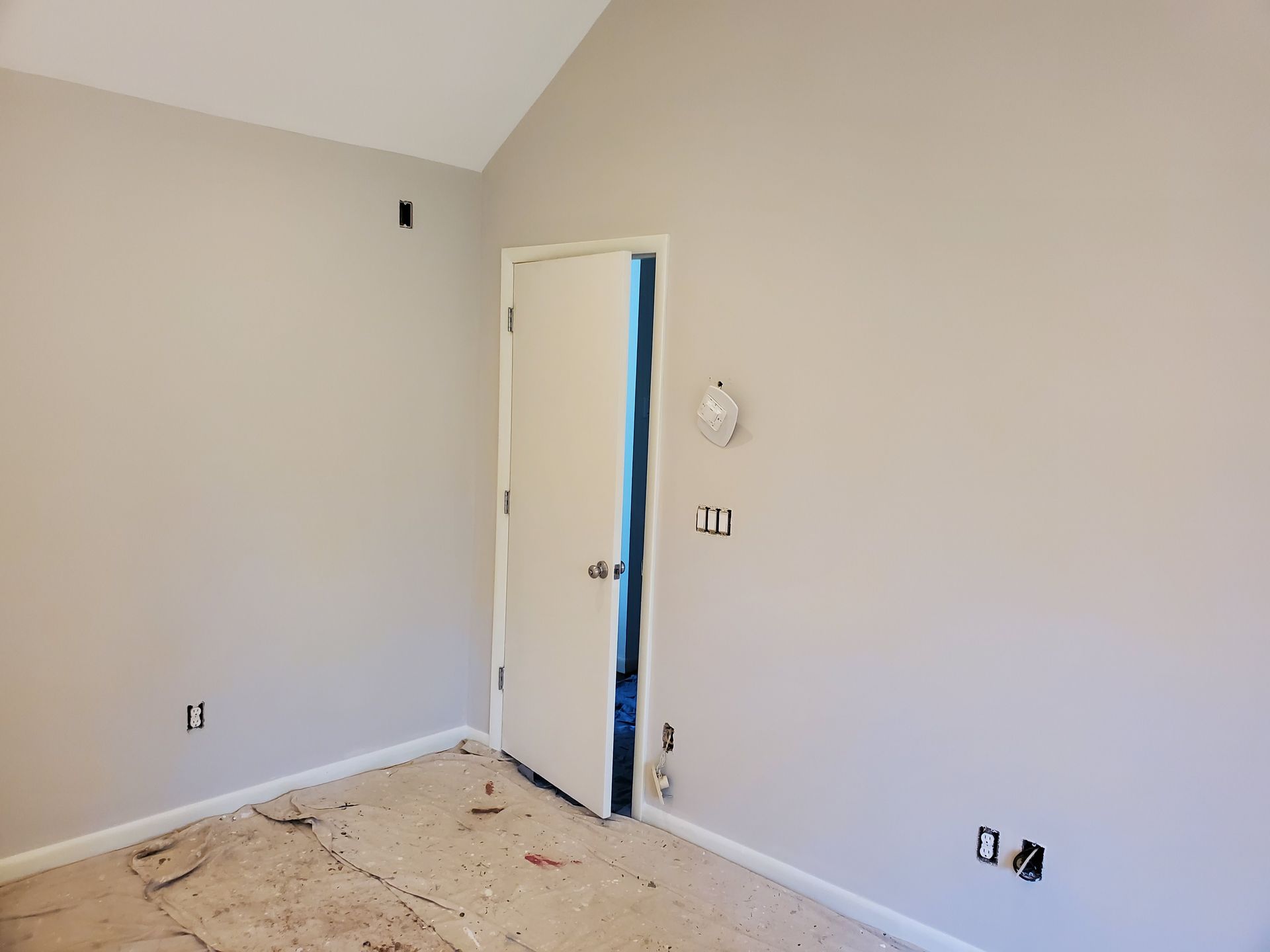 Worker plastering a white wall on a ladder in a room under renovation with building materials stacked nearby