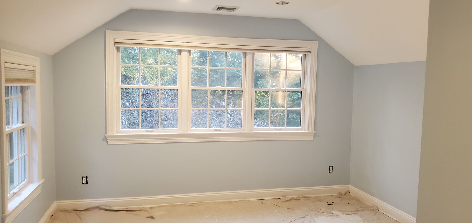 Painter in blue painting a ceiling with a roller, using protective coverings below.