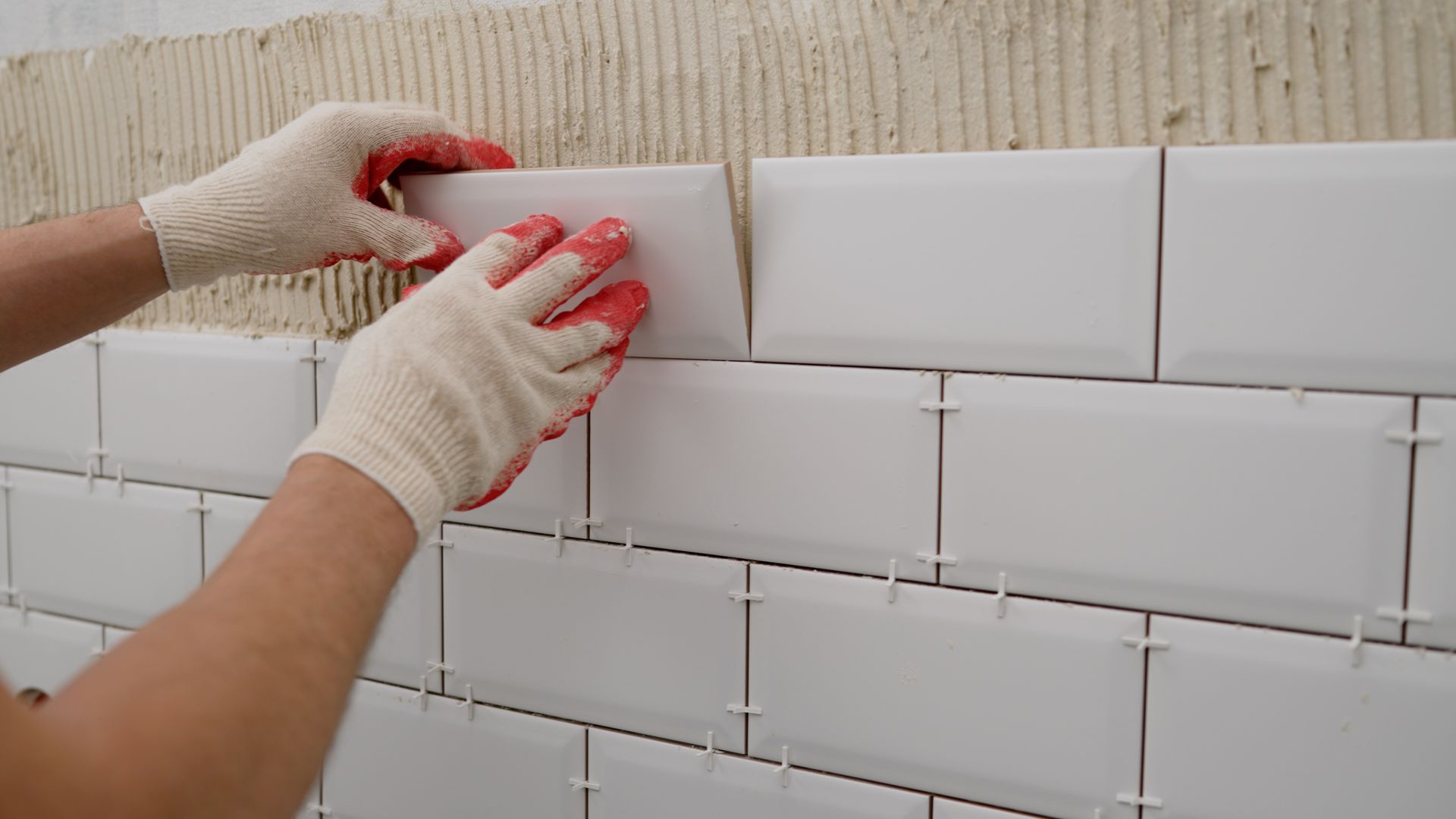 Worker smoothing plaster on a wall with a trowel, wearing white gloves and a blue shirt.