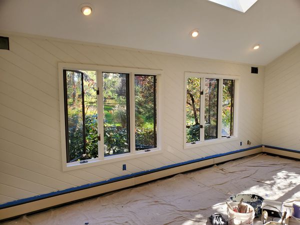 Hand painting a blue-walled living room with a roller, near a sliding glass door and wood floor