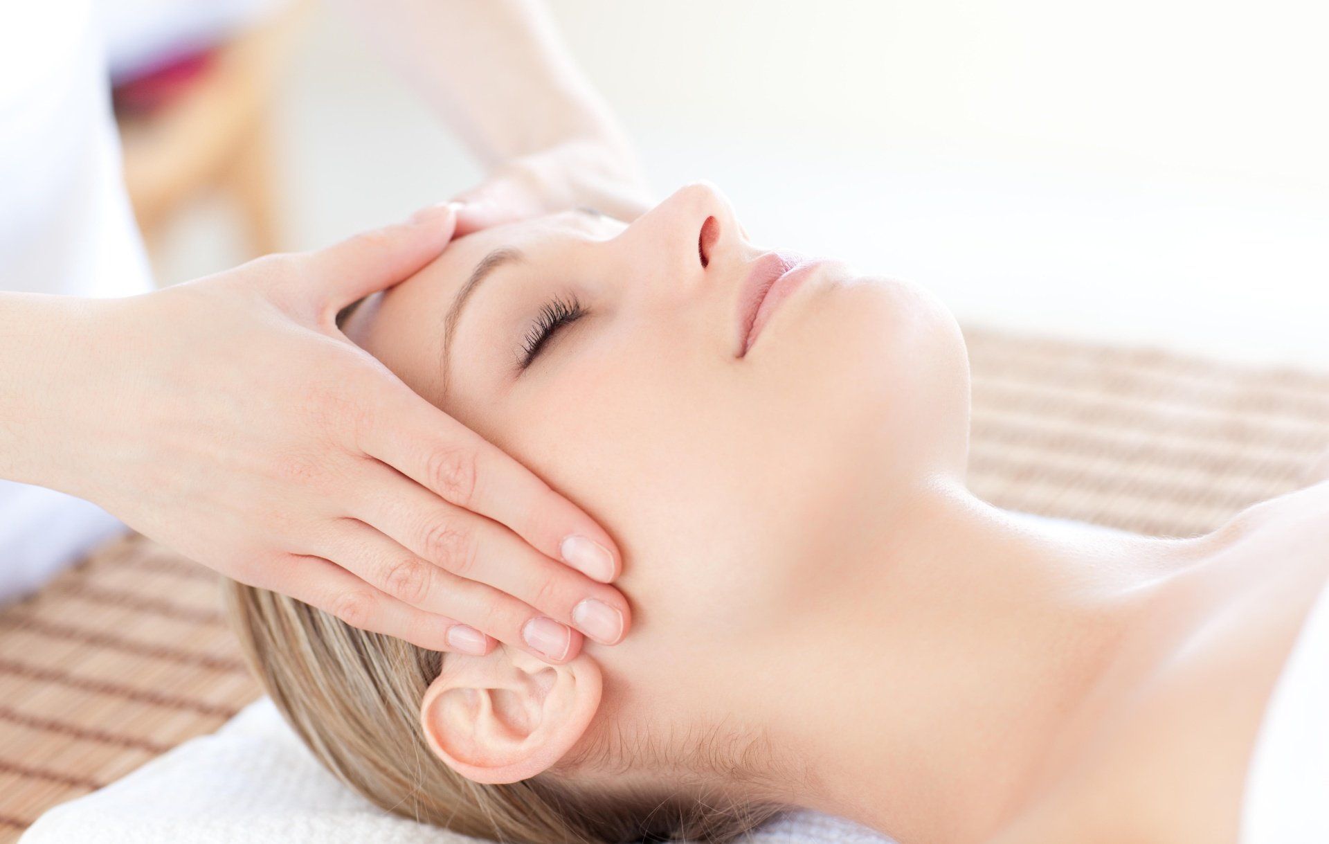Donna che riceve un massaggio facciale con gli occhi chiusi. Le mani le premono delicatamente il viso in un ambiente spa.