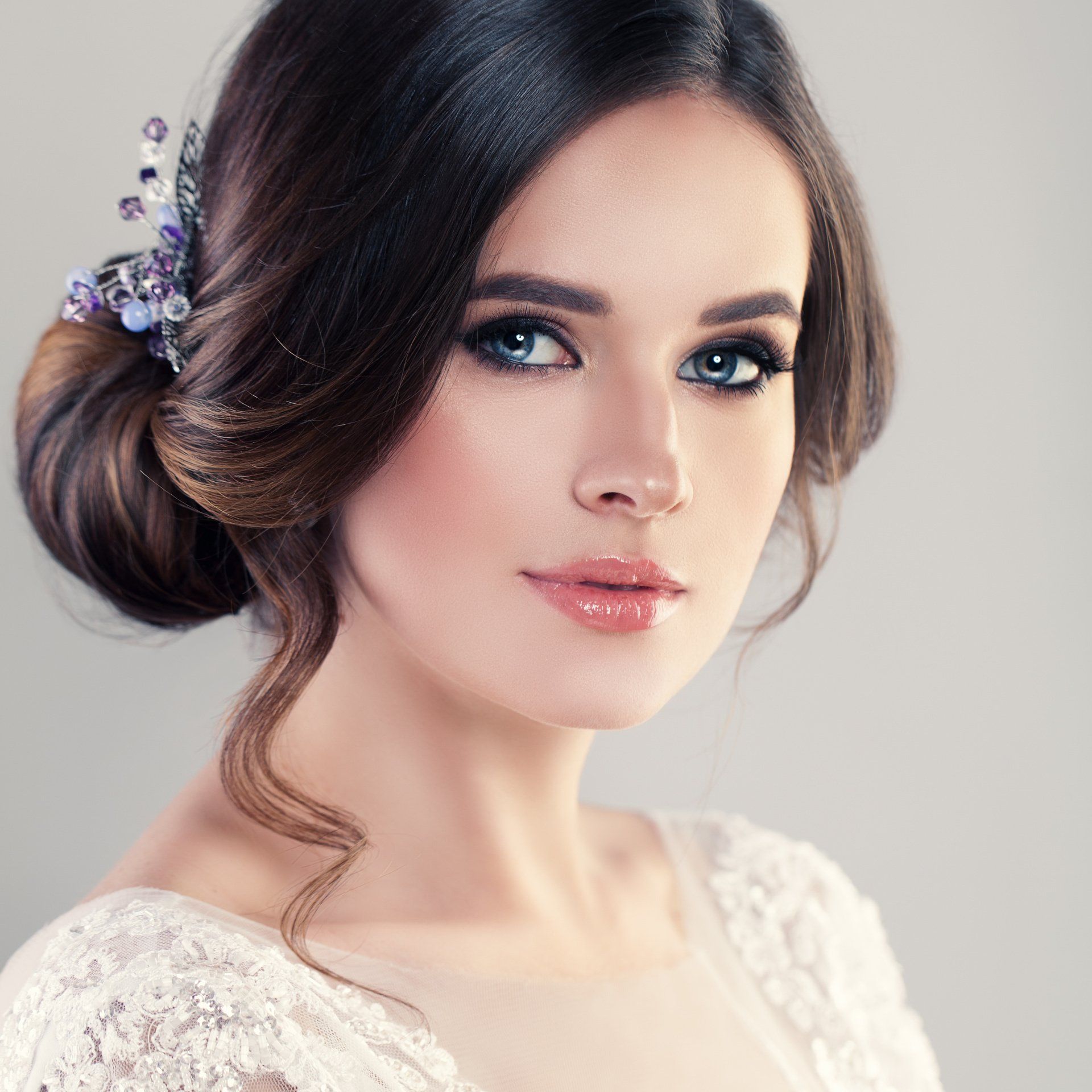 Donna con i capelli scuri raccolti in uno chignon, truccata e con un top in pizzo.