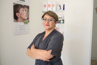 Donna con le braccia incrociate e gli occhiali in una clinica per la cura della pelle. Pubblicità sullo sfondo.