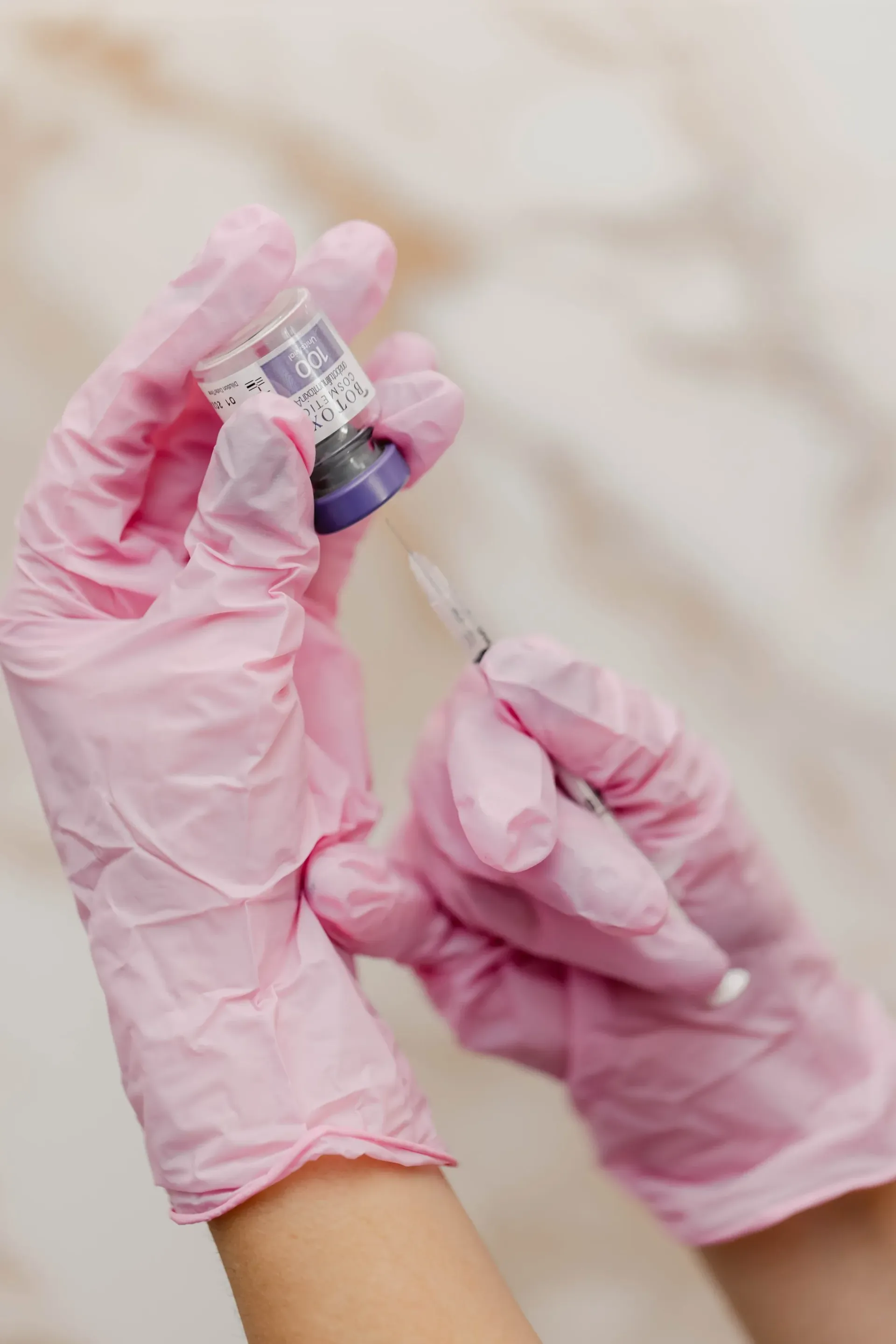 Pink-gloved hands holding a small vial and syringe in a medical setting