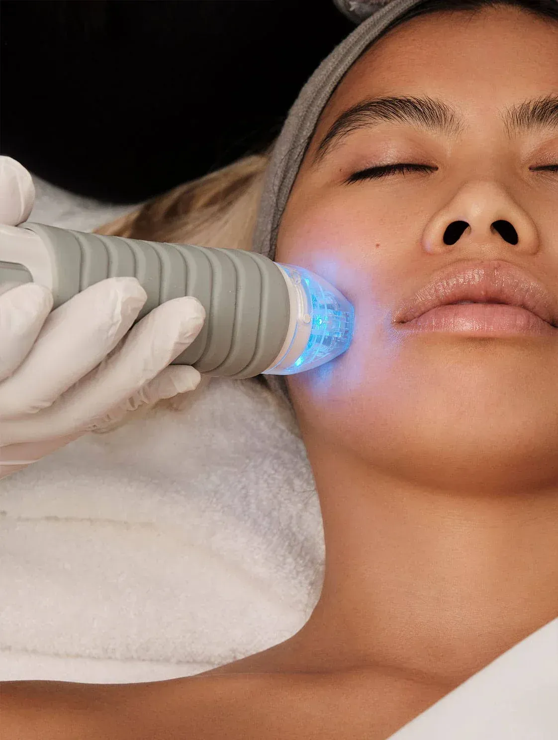 Gloved hand using a blue facial treatment device on a relaxed woman lying down