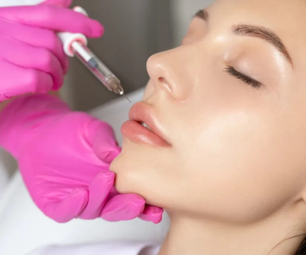 Gloved hands using a cosmetic tool on a woman’s cheek during a facial treatment