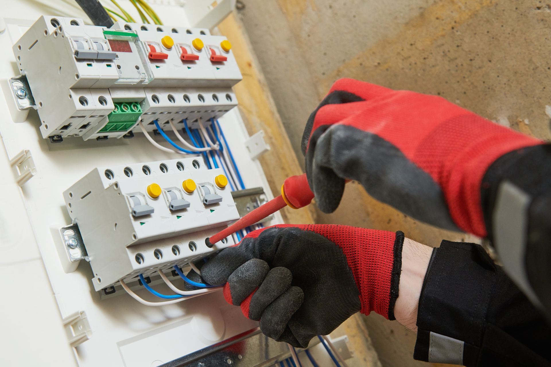Electrician in red gloves testing electrical panel with a voltage tester.