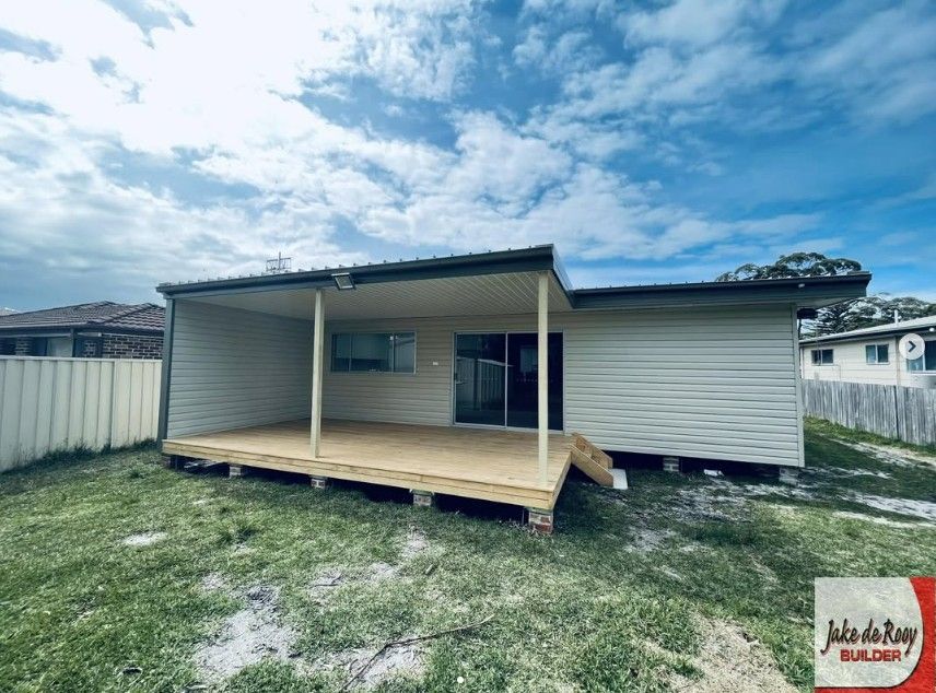 A light-colored house with a newly constructed wooden deck and covered patio area in a grassy backyard.