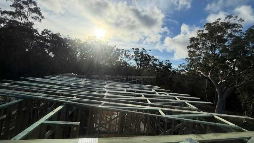 Metal roof framing of a house under construction during a bright, sunny day with trees in the background.