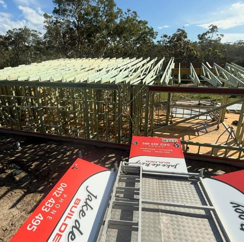 Wooden framing for a house under construction, viewed from above a Jake de Rey Builders branded site trailer.