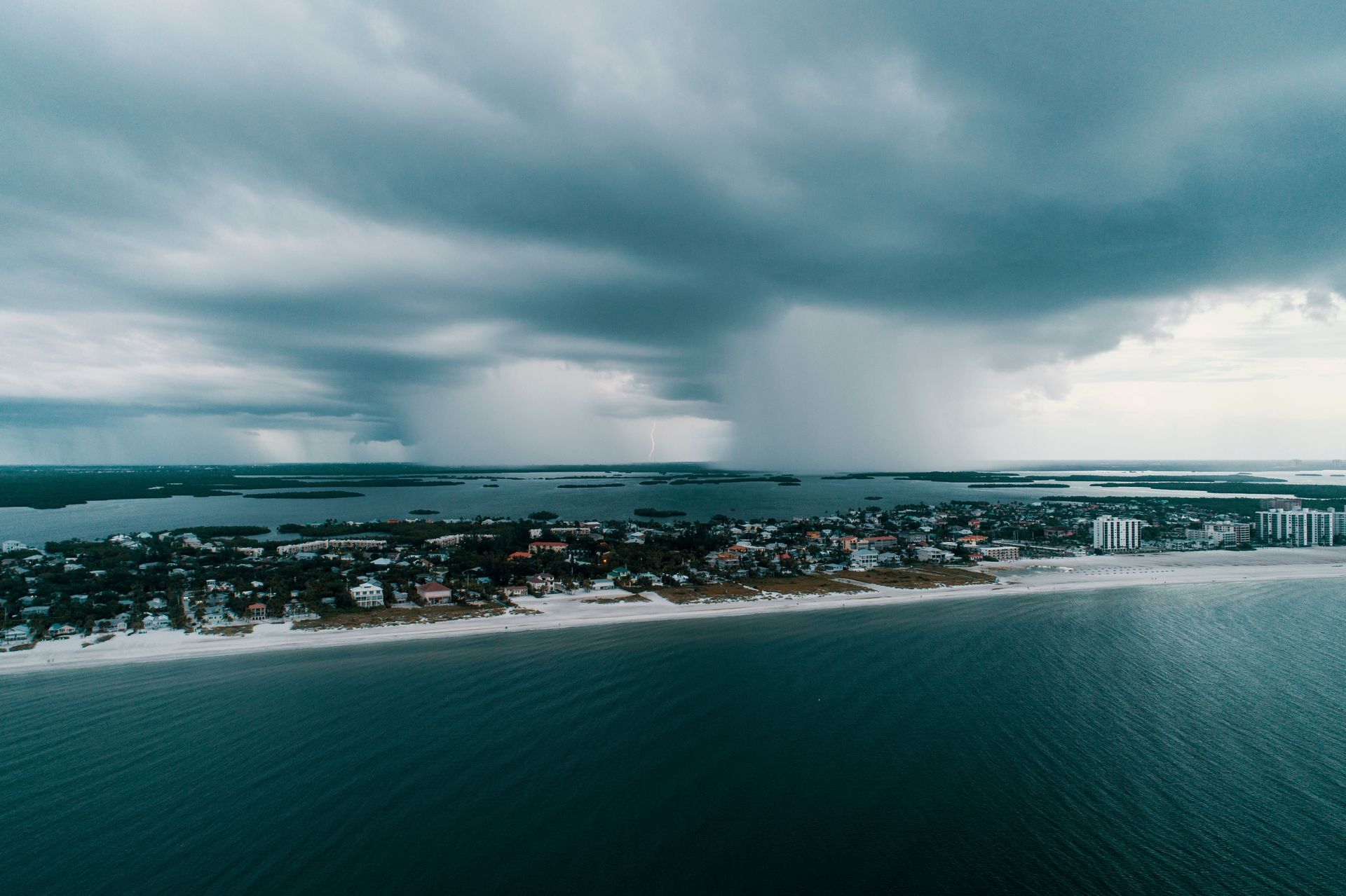 Storm clouds over a coastal town and shoreline beside dark blue water