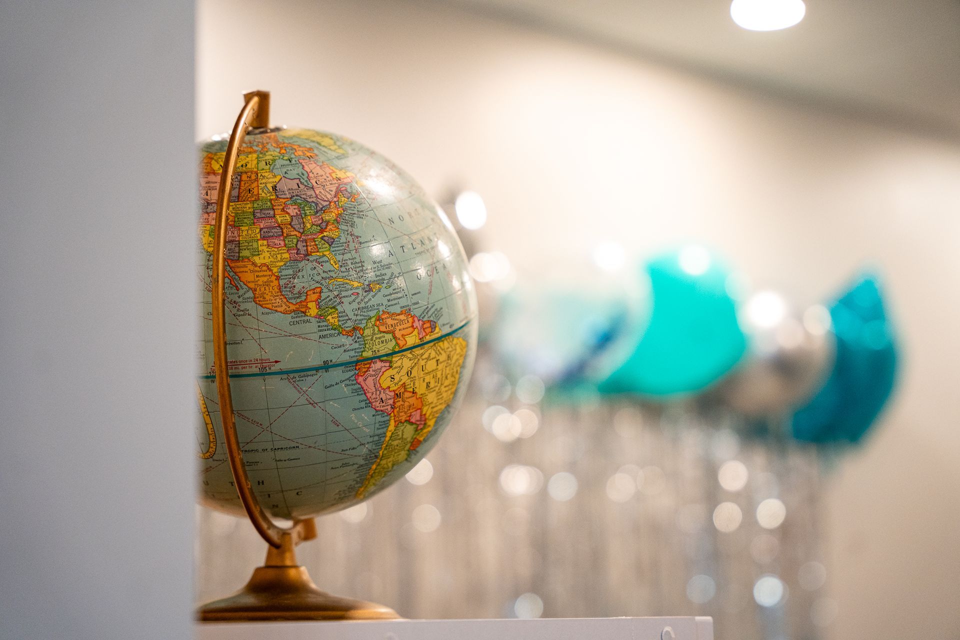Globe on a shelf in a softly lit room with teal balloons in the background