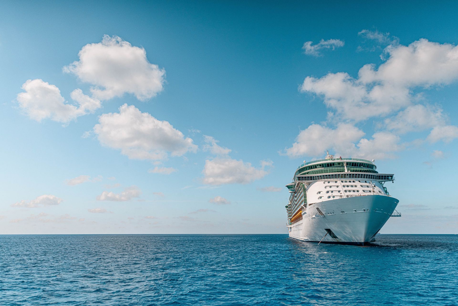 Large white cruise ship on calm blue ocean under a partly cloudy sky