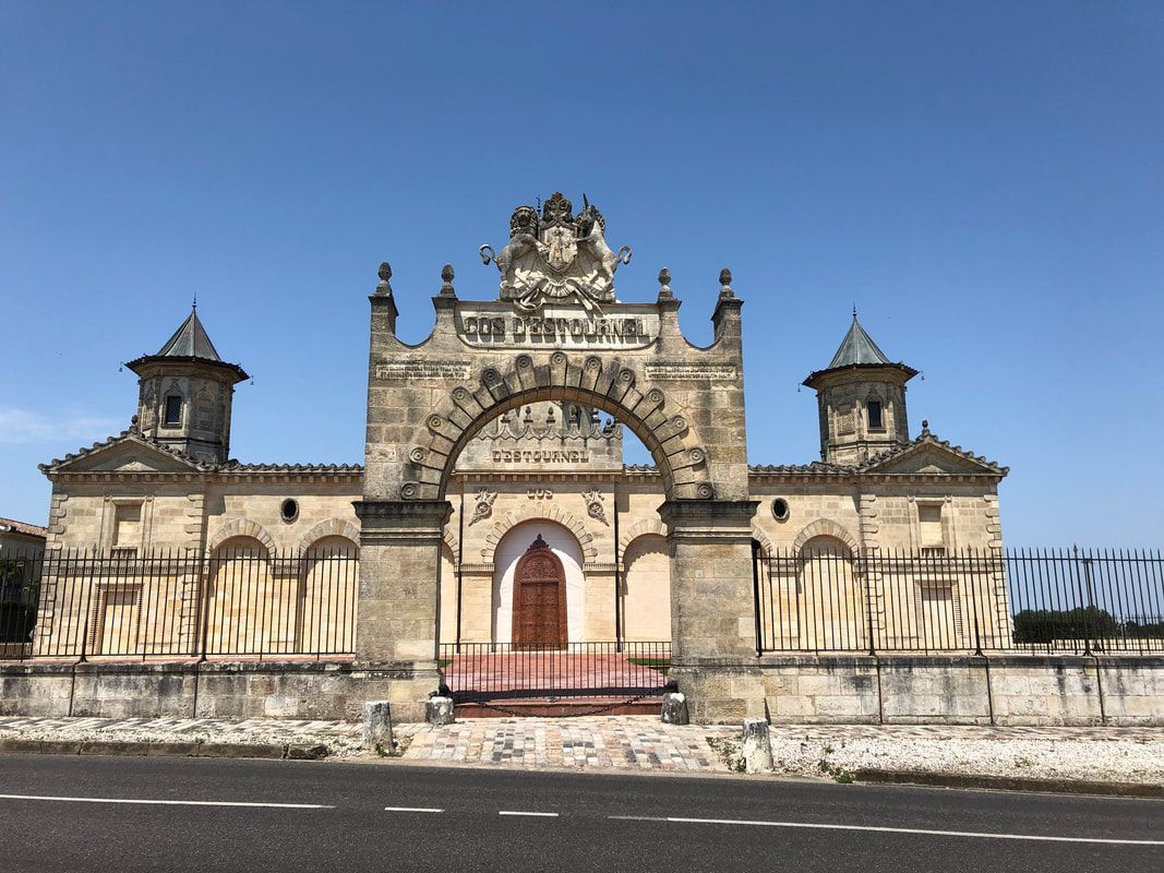 french chateau gate entrance A large stone building with a clock on the top of it is sitting on the side of a road.