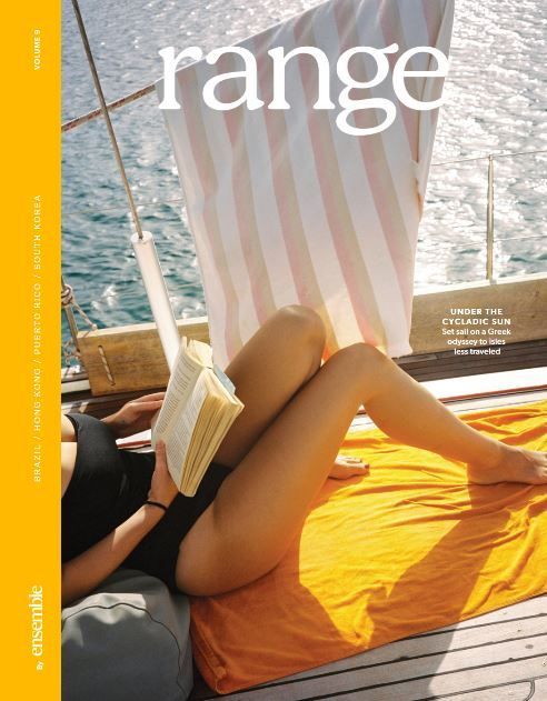 Person reading on a boat deck beside a striped curtain, with bright orange blanket and ocean view