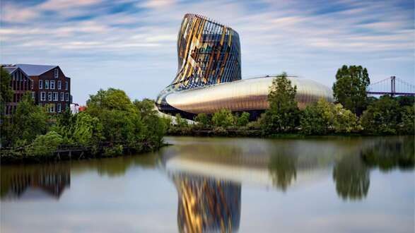 wine museum A large building is reflected in a body of water surrounded by trees.