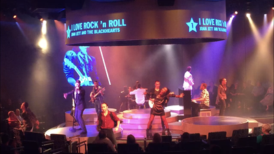 live music performance A group of people are standing on a stage in front of a large screen that says i love rock n roll.