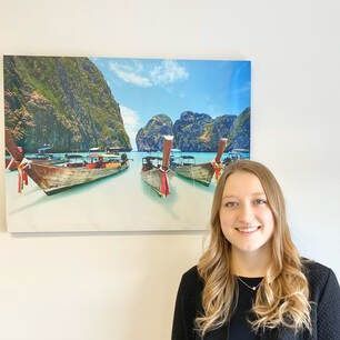 women in black shirt A woman is standing in front of a painting of boats in the ocean.