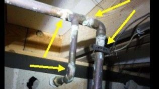 Copper pipes with visible white oxidation and corrosion at multiple soldered joints, marked by yellow arrows.