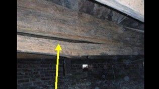 A yellow arrow points to a damaged, sagging wooden beam in a dark crawl space with a brick foundation.