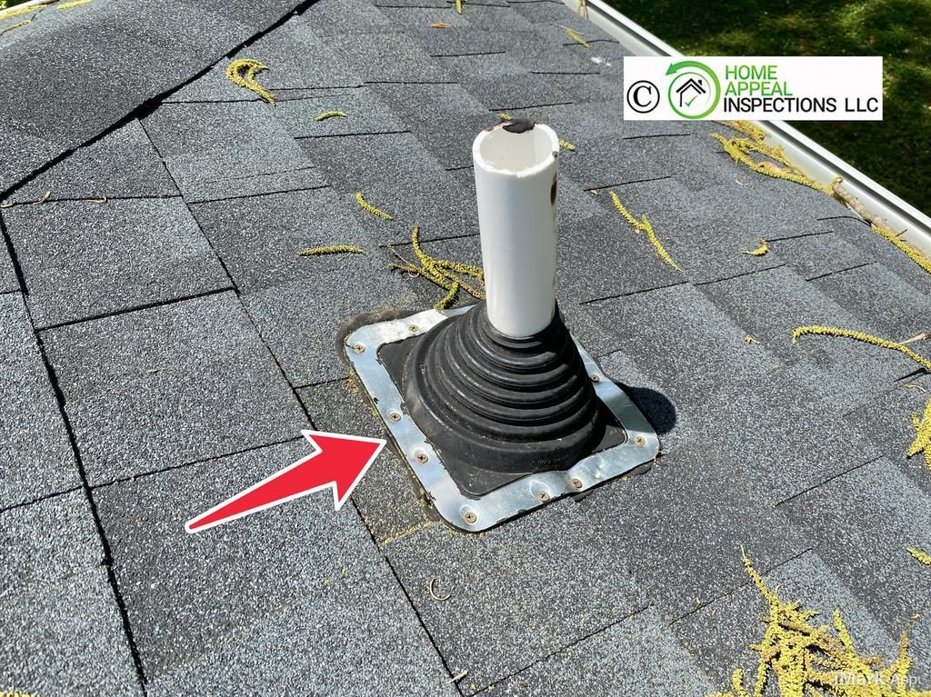 A roof vent pipe with a rubber boot flashing, marked by a red arrow, installed on gray asphalt shingles.