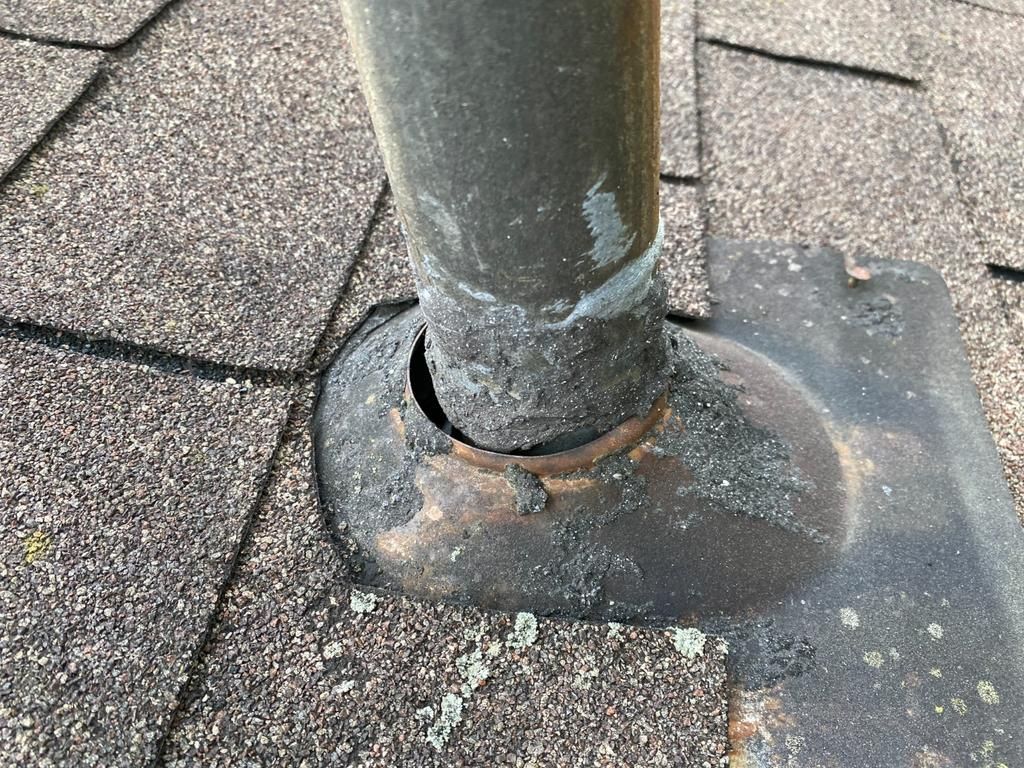 A roof vent pipe with a deteriorated rubber boot flashing, showing a visible gap where water can leak under the shingles.