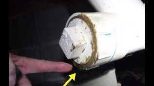 A finger points to a leak around the threads of a white PVC cleanout plug on a pipe.