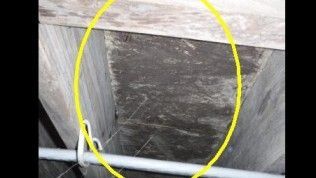 A close-up view of dark, textured material inside a wooden wall frame, circled in yellow for emphasis.