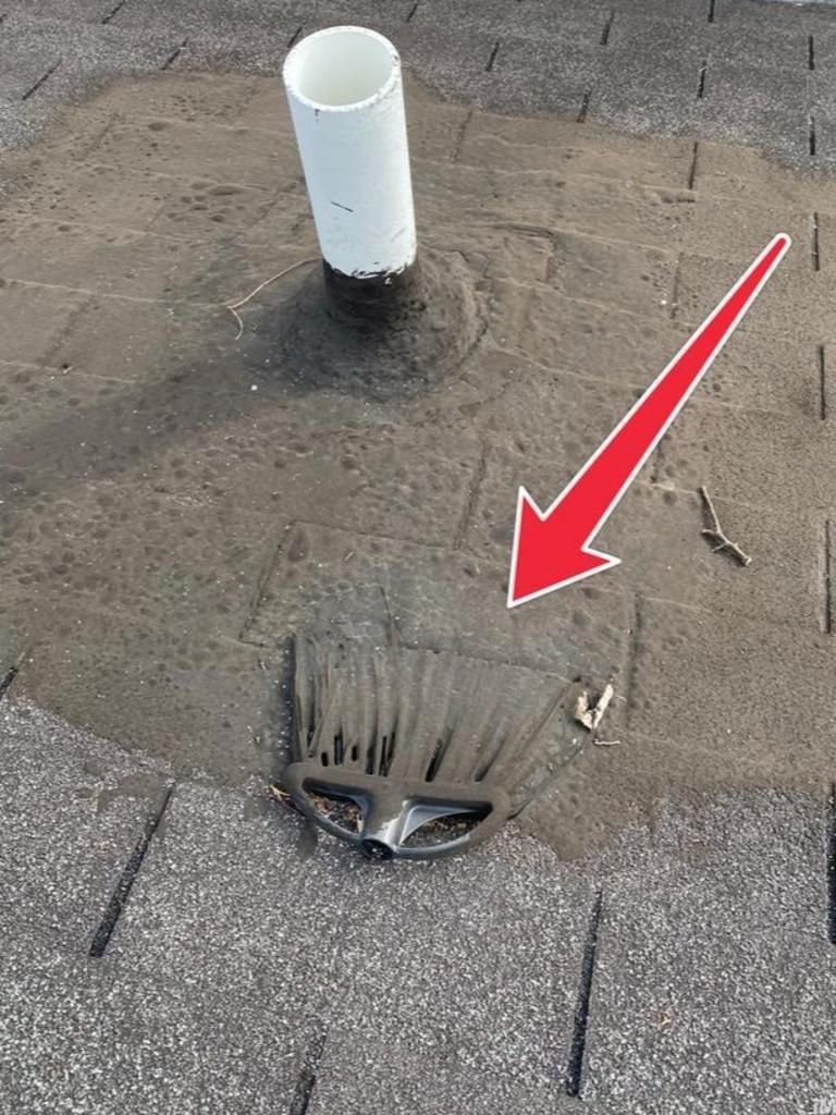 A broom head left on a grey shingled roof, pointing toward a white plumbing vent pipe with a red arrow overlay.