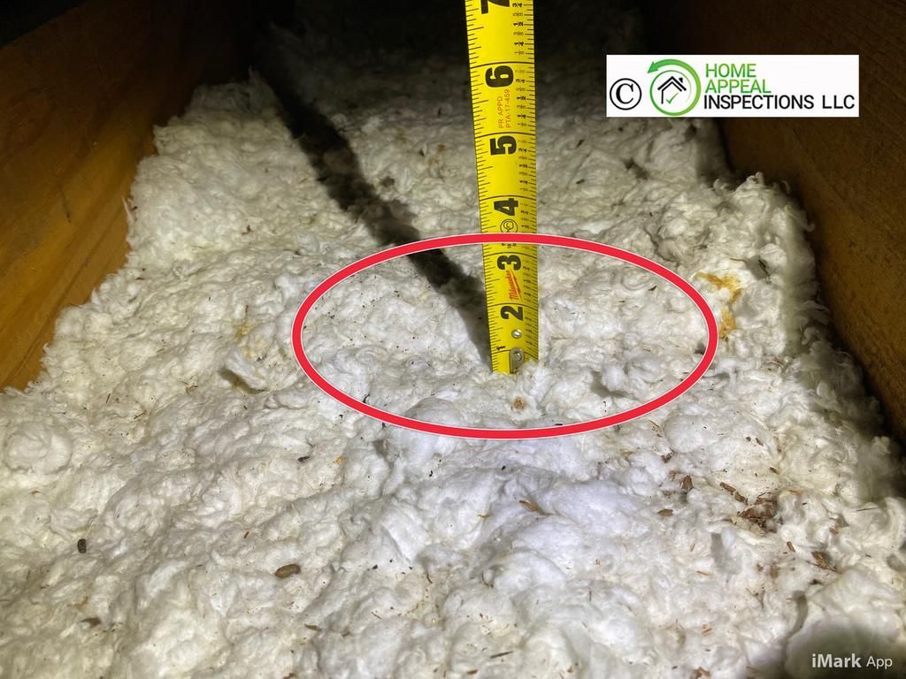 A tape measure inserted into white attic insulation, showing a depth of approximately three inches.