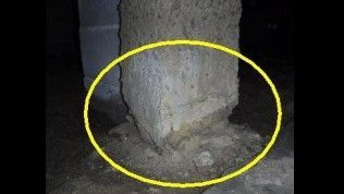 A concrete support pier in a dark crawl space, with a yellow circle highlighting crumbling material at its base.