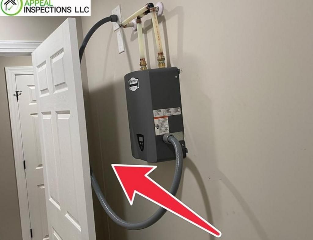 An electric tankless water heater mounted on a wall with a red arrow pointing to its power cable draped behind a door.