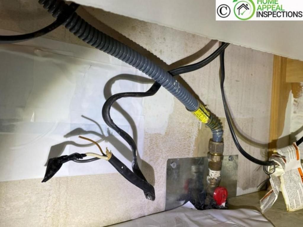 Exposed, uncapped electrical wires hanging near a gas shut-off valve under a cabinet.