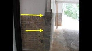 A partial wall with brick lower cladding and white upper paint, featuring yellow arrows pointing to a vertical joint.