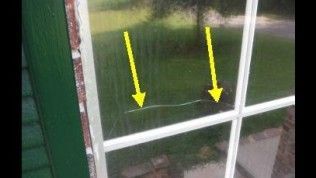 A window pane with a horizontal crack, highlighted by two yellow arrows pointing toward the damage.