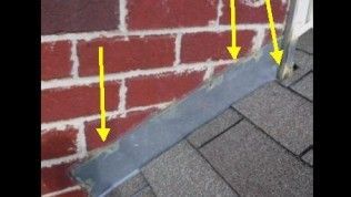 Yellow arrows point to sealant on metal flashing where it meets a red brick wall above asphalt roof shingles.