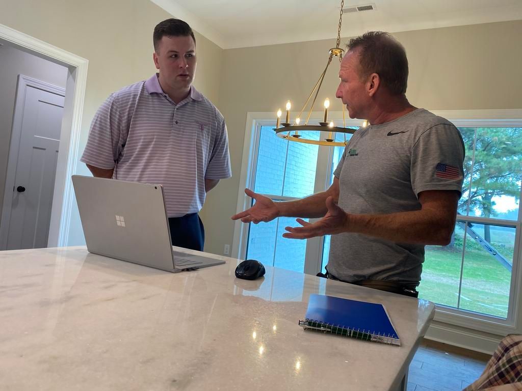 Two professionals stand at a marble kitchen island, discussing information on a laptop and a blue folder.