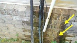 Brick wall showing moisture damage and dark staining near exposed pipes, with yellow arrows pointing to the discolored area.