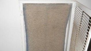 A heavily dust-covered HVAC air filter sits inside a wall-mounted vent.