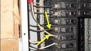 An electrical panel with yellow arrows pointing to white wires incorrectly connected to the hot terminals of breakers.