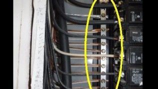 Electrical panel interior with a yellow oval highlighting a neutral/ground bar connected to several wires.