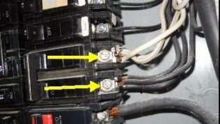 Close-up of a circuit breaker panel with yellow arrows pointing to two wires improperly double-tapped into one terminal.