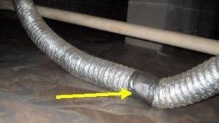 Flexible silver ducting in a crawlspace connected with gray duct tape, indicated by a yellow arrow.