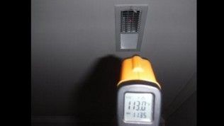 A hand-held infrared thermometer pointed at a ceiling air vent shows a temperature reading of 113.0 degrees Fahrenheit.