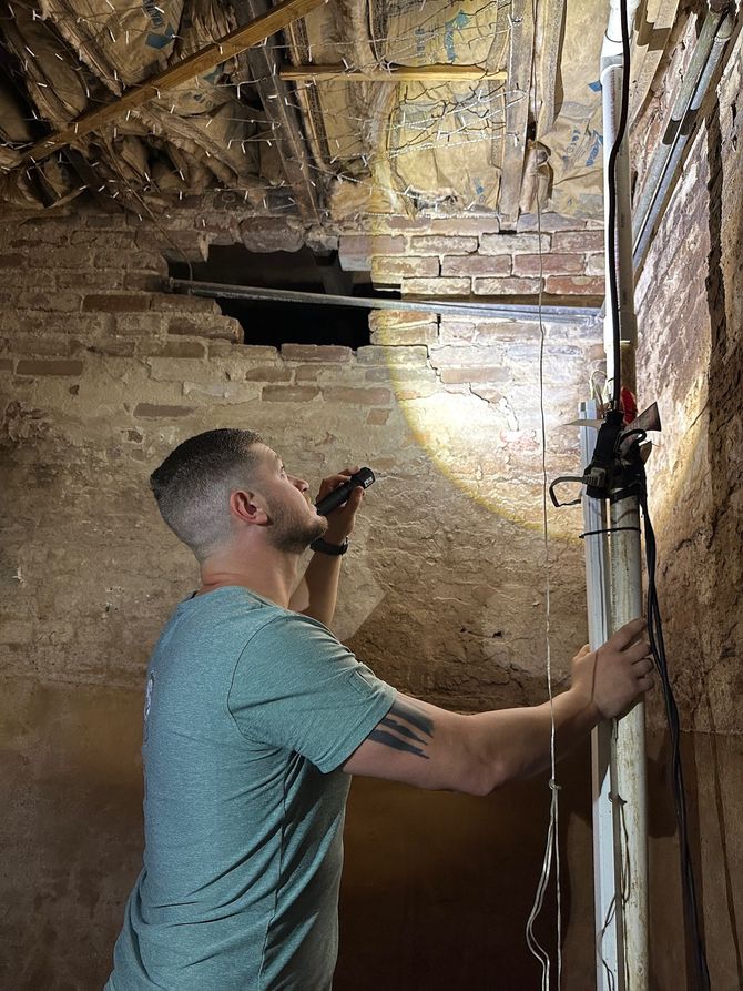 Worker inspecting an old brick ceiling with a flashlight in a dim room