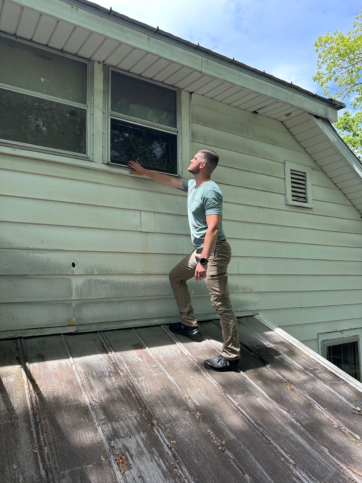 Person inspecting an open window from a sloped roof on the side of a house.