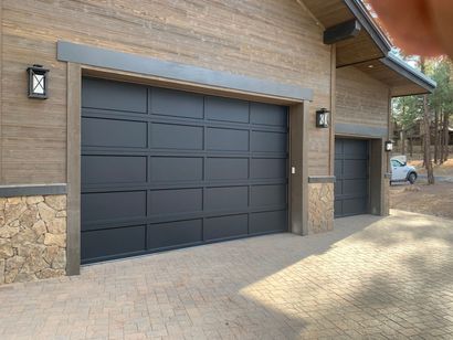 A modern house exterior featuring a two-car and a one-car garage with dark, paneled doors and stone accents.